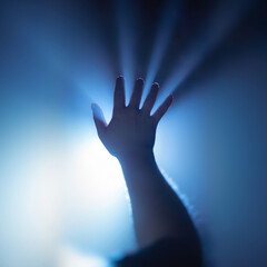 The girl stretches her hand to a source of bright light in the fog, the rays break through her fingers. Mystic atmosphere