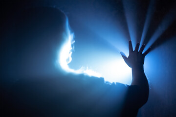 The girl stretches her hand to a source of bright light in the fog, the rays break through her...