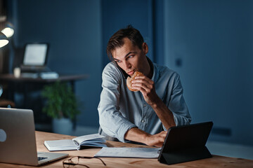 young businessman snacking on a hamburger while working on a new project.