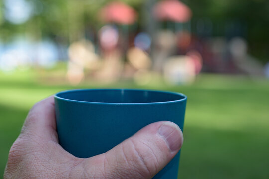 Shot of hand holding a drink while I watch my grandkids playing on the playground equipment at Cole Park in Upstate NY.  Memorial Day Picnic in Broome County.
