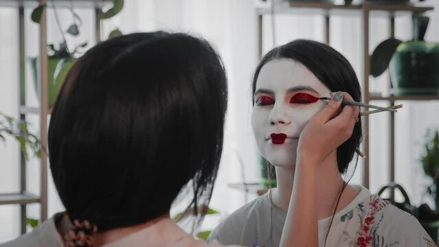 A young woman creates the image of a geisha for a girl. Makeup. Creating an image for an event