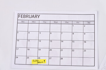 February calendar and slow down note on white background. Laziness day concept.