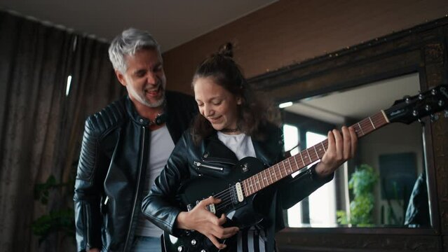 Father rock guitarist having fun and and dancing with his teenage daughter at home.
