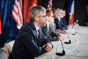 Group of people sitting at table in front of microphones in a row and answering questions during...