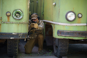 Military man hide in position between old rusty busses with weapon in hands. Shooter with gun...