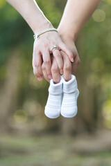 Future parents holding hands and a pair of newborn baby shoes with isolated blur garden background