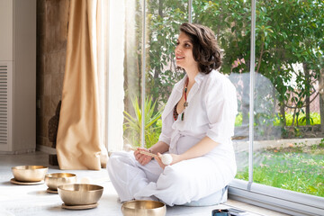 Beautiful woman sitting on the floor with sound bowls on garden background, sound healing therapy