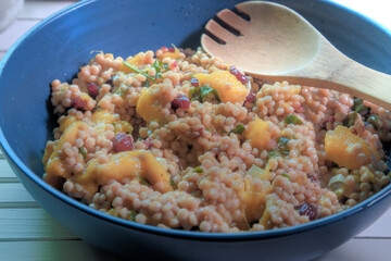 Side view of mango couscous salad on white natural wood table