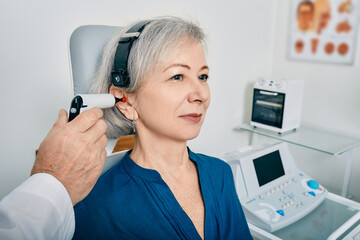Elderly woman receives tympanometry with tympanometer probe at hearing clinic. Hearing check-up, impedance audiometry