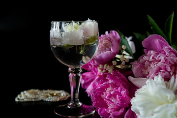 wine and flowers. still life with flowers. Bouquet of white and pink peony on a black background. Pearl necklace. Flower in a glass of water