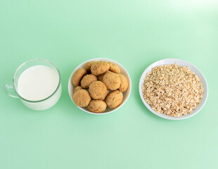 Flat lay white milk, oatmeal, and oatmeal cookies on a white plate on a green background, top view, the concept of healthy eating and preparing a healthy breakfast. Quality photo. High-quality photo
