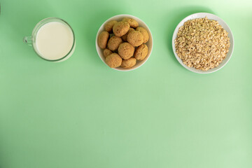 Fototapeta na wymiar Flatlay white milk, oatmeal, and oatmeal cookies on a white plate on a green background, top view, the concept of healthy eating and preparing a healthy breakfast.Place for text below