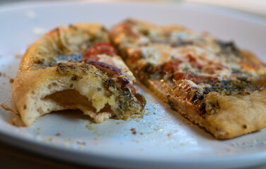 Side view and closeup of vegetarian pesto pizza on white plate.
