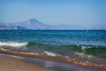 Sea in sunny weather. Waves. Mountains on the horizon. Alicante