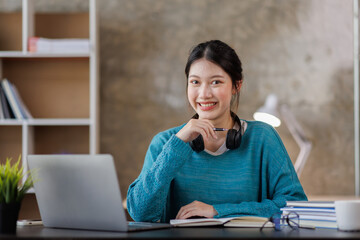 Young attractive female student writer scribing notes to a textbook to prepare for the  Exam preparation, Asian girl sitting homework on a laptop computer, making a plan for tomorrow creating a list