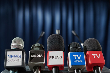 Close-up of microphones of different tv media in front of tribune for speaker at press conference