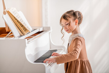 A little girl plays a big white piano in a bright sunny room