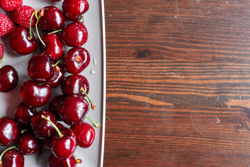 A full plate of juicy, bright pink freshly washed cherries. Wet raspberries. A plate of summer vitamins. Space for text.