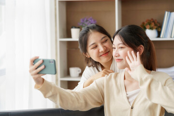 Asian lesbian couple, LGBTQ. Lesbian couple holding smartphone and posing while making selfie together. Happy two young Asia women showing love and romance together at home.