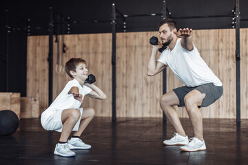 Healthy family concept. Father trainer and teenager son training with dumbbells in the gym....