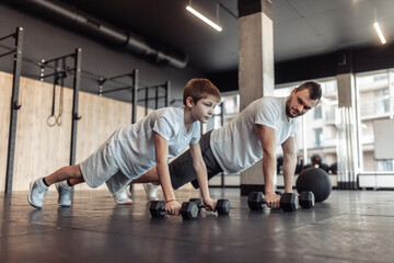 Fototapeta na wymiar Healthy family concept. Father trainer and teenager son push ups with dumbbells in gym. Fitness, sports, active lifestyle