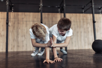 Two teenagers do push-ups and high fives in the gym. Children's fitness