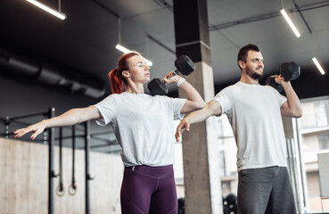 Athletic man and woman doing intensive workout together with dumbbells in a modern gym. Functional training. Bodybuilding and fitness. Healthy lifestyle