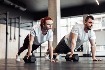 Fototapeta na wymiar Athletic man and woman doing intensive workout together with dumbbells in a modern gym. Functional training. Bodybuilding and fitness. Healthy lifestyle