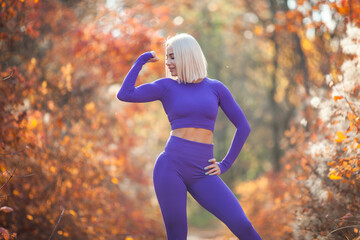 Muscular young woman athlete posing in autumn forest