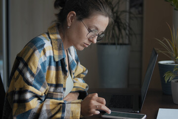 Close-up of brunette woman, in round eyeglasses working at her desk in a home office. Millennial young woman works and use her smartphone. A Girl Is Concentrated Browsing Smartphone