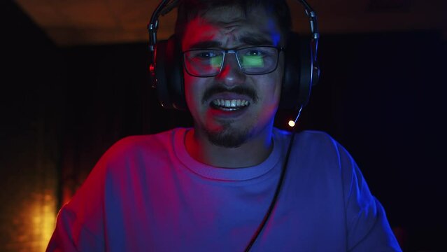 Male gamer playing games on computer and grimacing with irritation, front view. Male nerd gamer plays video games with an annoyed look