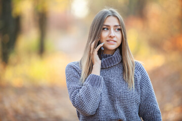 Cute young woman in warm sweater talking on the phone in autumn forest
