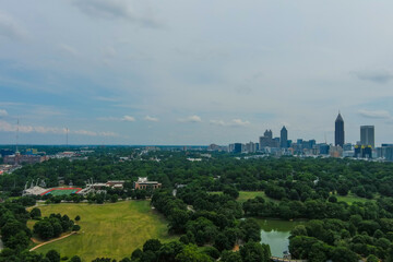 Fototapeta na wymiar a stunning aerial shot of the skyscrapers and office buildings in the city skyline with lush green trees, grass and plants and a green lake and blue sky with clouds at Piedmont Park in Atlanta 