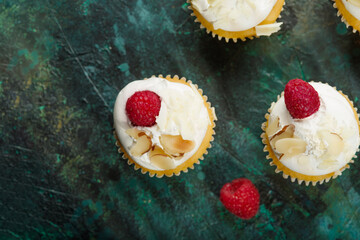 Light delicious dessert - muffins with cream, fresh raspberries and almond flakes. Isolated on a dark green background. View from above. Birthday, anniversary, romantic date.