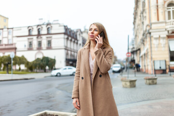 Young beautiful woman in a coat talking on the phone in European city