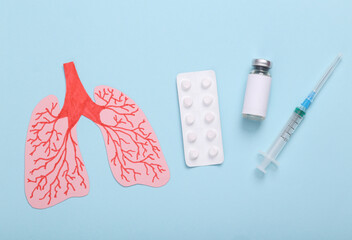 Vaccination, treatment for lung disease, covid 19 or pneumonia. Paper cut anatomical lungs with a bilster of pills, a bottle of vaccine and a syringe on a blue background. Top view