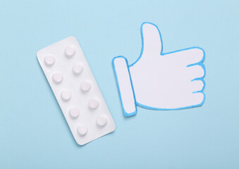 Blister of pills with thumb up icon on blue background