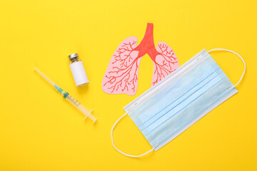 Vaccine bottle with syringe, medical mask and anatomical lungs on a yellow background. Pandemic covid 19