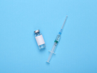 Vaccine bottle with a blank label for the brand and syringe on blue background.