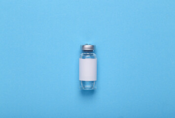 Vaccine bottle with a blank label for the brand on blue background. Top view