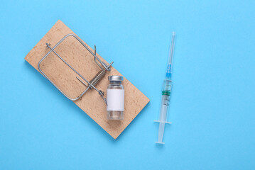 Mousetrap with a bottle of vaccine and a syringe on a blue background