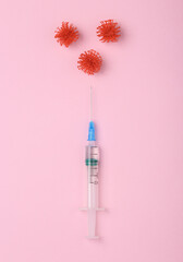 Vaccination against covid 19. Syringe with virus molecules on a pink background