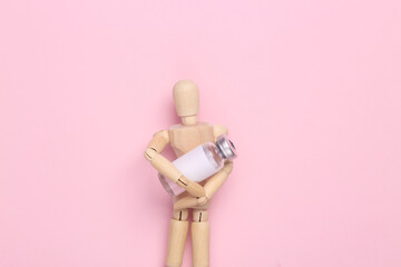 Wooden Puppet holding bottle vaccine on pink background