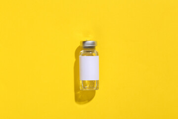 Vaccine bottle with blank label on yellow bright background. Top view