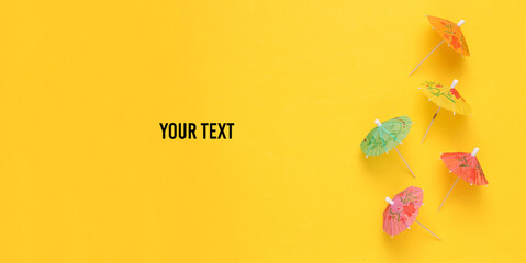 Mini cocktail umbrellas on yellow background. Summer background. Top view. Copy space