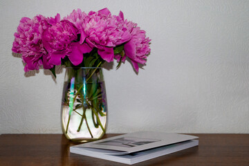 Pink peonies. Bouquet of pink peonies in a vase on a brown table against a white wall.
Selective focus.