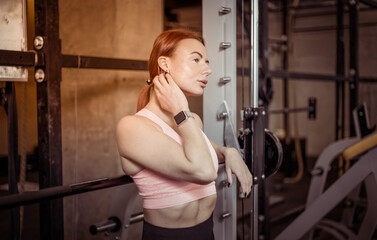 Fototapeta na wymiar Attractive fit slim red-haired woman in sportswear resting leaning on barbell in modern gym