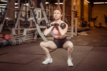 Fototapeta na wymiar Intensive workout red-haired woman with kettlebells in her hand in modern gym