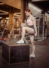 Fit woman in sportswear steps on a wooden box with a kettlebells in her hands in the gym. Intensive functional training