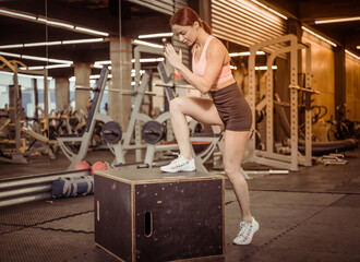 Fit woman in sportswear steps on wooden box in the gym. Intensive functional training